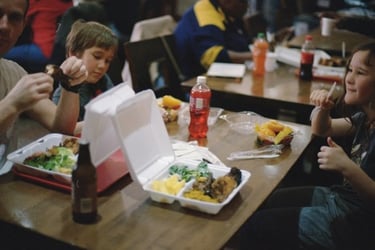 Students eat lunch at a table with meals in to-go containters.