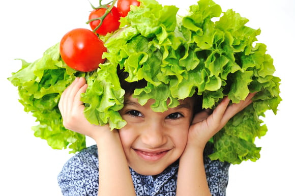 Kid with salad and tomato hat on his head, fake hair made of vegetables