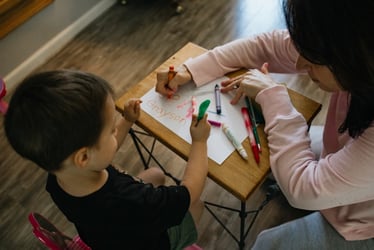 Preschool boy writing his name on paper with markers and other supplies