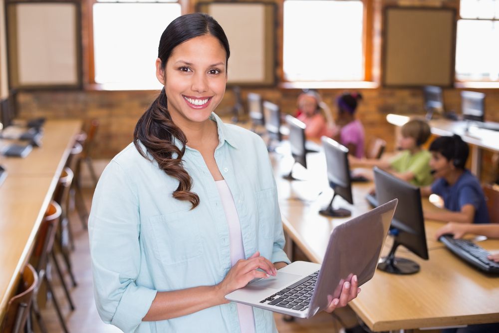 Pretty teacher using laptop in computer class at the elementary school-1
