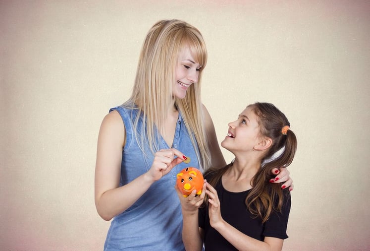 Closeup portrait young smiling girl holding piggy bank, happy mother, older sister deposits money isolated light black background. Smart financial investment wealth decisions. Budget management saving