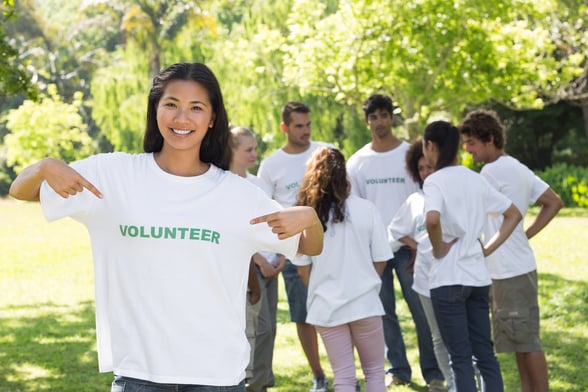 Portrait of beautiful volunteer pointing at tshirt with friends in background