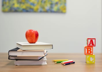 Books, an apple, crayons and blocks sit on a desk.