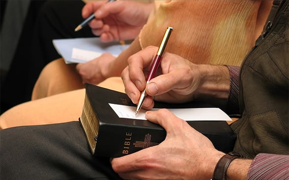Man in church writing down sermon notes on Bible about giving and stewardship